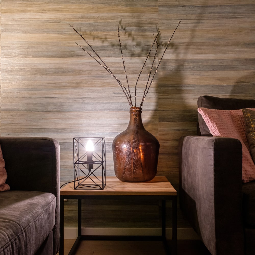 Oude messing vaas met takken, gezellige woonkamer met zachte bank, Lichy Lampen in Scandinavische stijl, decoratieve tafelverlichting voor sfeervolle interieuraccenten, perfecte verlichting voor modern huis.