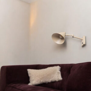 Minimalistische witte wandlamp boven een paarse bank met een crème kussen, stijlvolle interieurverlichting van LICHY LAMPEN, modern en functioneel design, perfecte sfeerlicht voor woonkamer en zithoek.